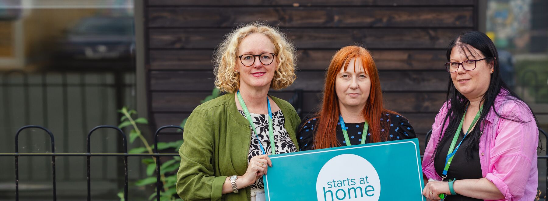 Three people holding a sign which reads 'starts at home'