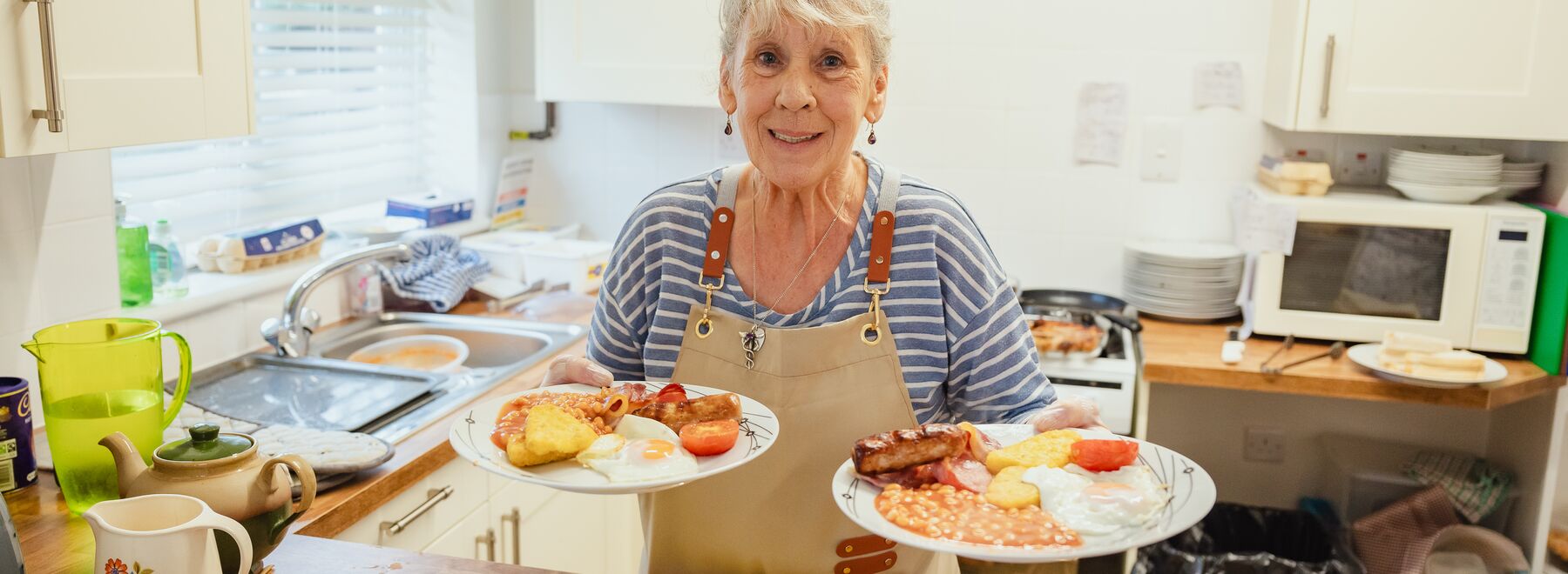 A woman holding two plates of cooked breakfast