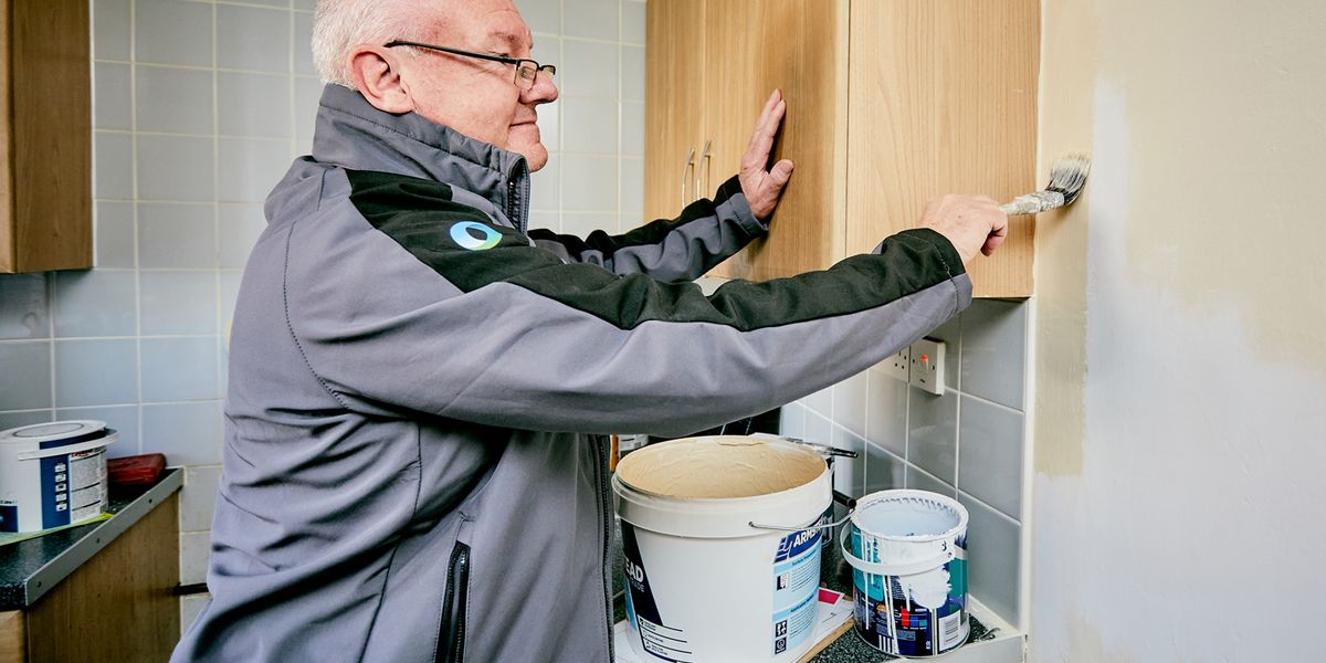 Male tradesperson painting a wall standing next to pots of paint