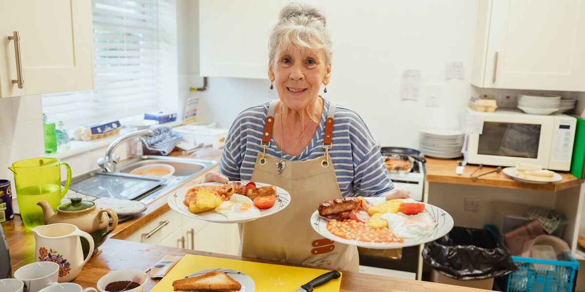 A woman holding two plates of cooked breakfast