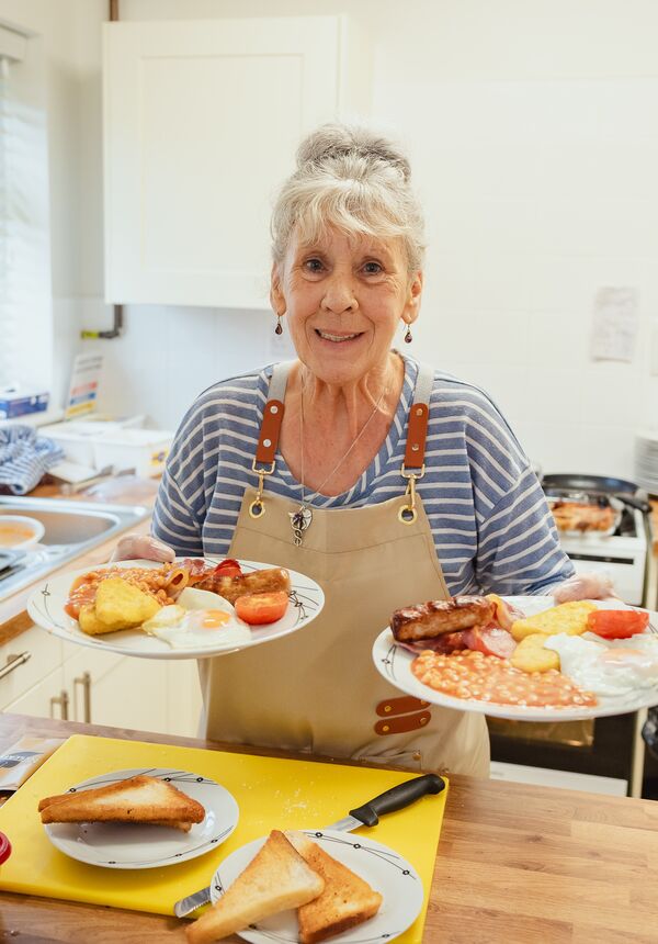 A woman holding two plates of cooked breakfast