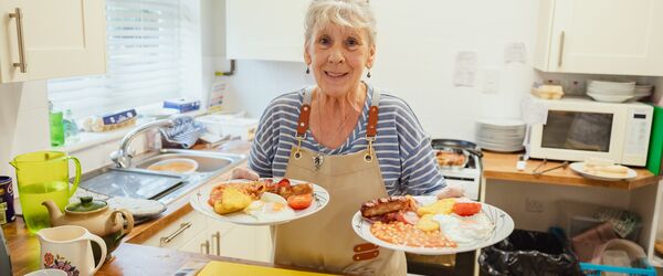 A woman holding two plates of cooked breakfast