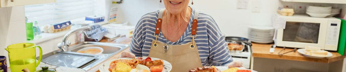 A woman holding two plates of cooked breakfast