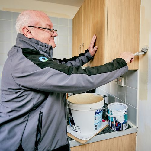 Male tradesperson painting a wall standing next to pots of paint