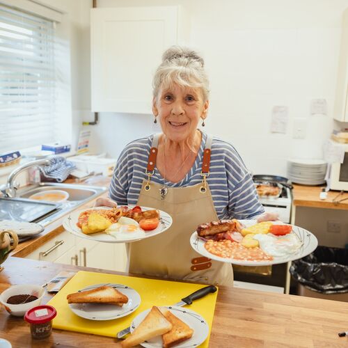 A woman holding two plates of cooked breakfast